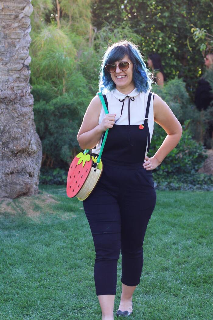 Andrea with blue hair, a white collared top, and a strawberry purse