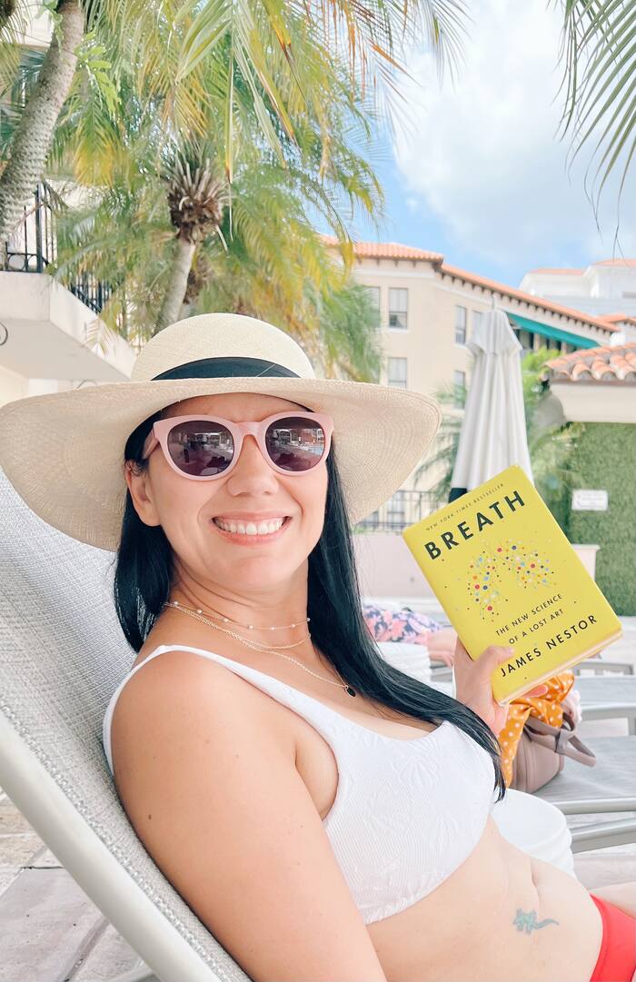 A woman in a sun hat reading the book Breath by the pool
