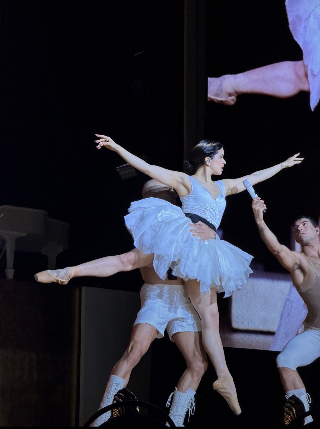 Rosalía en pointe in a white tutu, lifted by a dancer on stage during her LUX concert